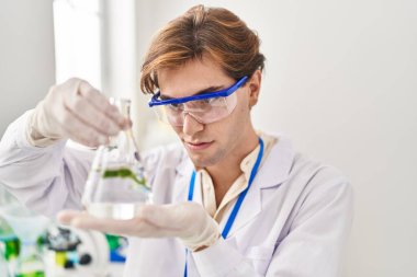 Young caucasian man scientist holding test tube with plant at laboratory
