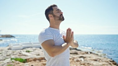 Genç İspanyol adam plajda yoga egzersizi yapıyor.