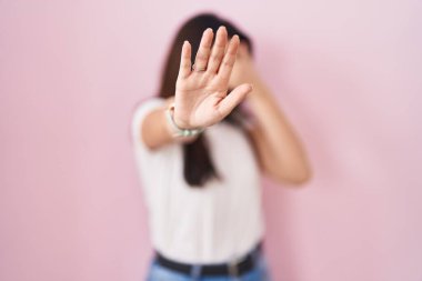 Young brunette woman standing over pink background covering eyes with hands and doing stop gesture with sad and fear expression. embarrassed and negative concept. 