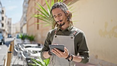 Genç İspanyol garson, kahve dükkanının terasında ciddi yüzlü dokunmatik ped kullanıyor.