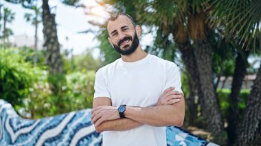 Kollarını kavuşturup parkta gülümseyen İspanyol genç adam.