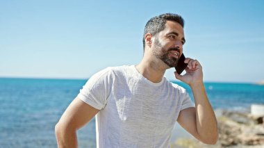 Genç İspanyol adam gülümsüyor. Sahilde akıllı telefondan konuşuyor.