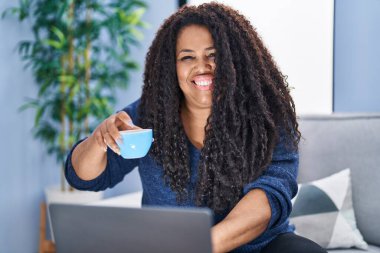 African american woman using laptop drinking coffee at home