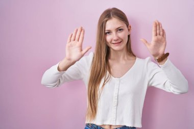 Young caucasian woman standing over pink background showing and pointing up with fingers number ten while smiling confident and happy. 