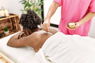 Afro-Amerikalı kadın güzellik salonunda tuz kullanarak sırt masajı yaptırıyor.