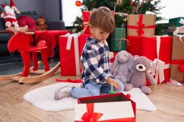 Sevimli İspanyol çocuk evdeki Noel ağacının yanında yerde oturmuş çember oyuncağıyla oynuyor.