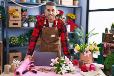 Young caucasian man florist smiling confident using laptop at flower shop