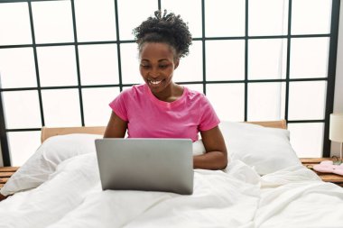 Yatak odasında dizüstü bilgisayar kullanan Afrikalı Amerikalı bir kadın.