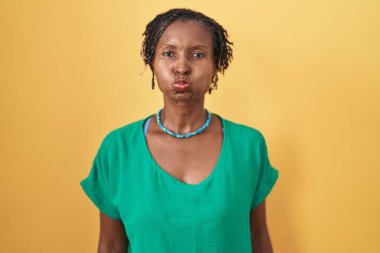 Sarı arka planda duran sarı saçlı Afrikalı kadın komik yüzlü yanakları şişiriyor. Havayla şişmiş ağız, çılgın bir ifade.. 
