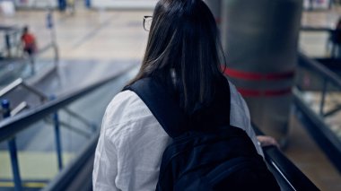 Genç ve güzel İspanyol kadın tren istasyonunda yürüyen merdivende sırt çantası takıyor.