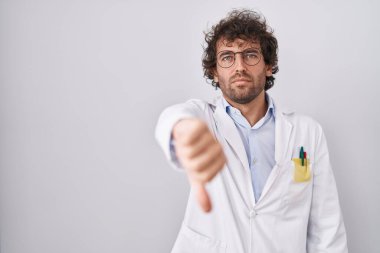 Doktor üniforması giyen İspanyol genç adam mutsuz ve kızgın görünüyor. Reddedilmiş ve olumsuz bir hareket sergiliyor. kötü ifade. 