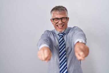 İspanyol iş adamı, gri saçlı, gözlüklü, seni ve kamerayı işaret eden, pozitif ve neşeli gülümseyen. 