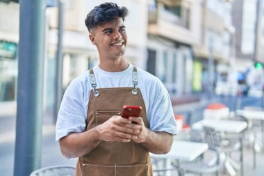 Genç İspanyol garson, kahvecinin terasında akıllı telefon kullanarak gülümsüyor.