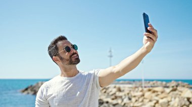 Genç İspanyol turist gülümsüyor. Kendine güveni tam. Sahilde akıllı telefondan selfie çekiyor.