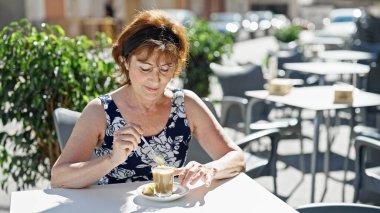 Orta yaşlı kadın kahve dükkanının terasında kahveyi karıştırıyor.