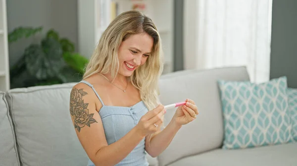 Young blonde woman smiling confident holding pregnancy test at home