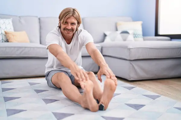 Young blond man smiling confident stretching leg at home