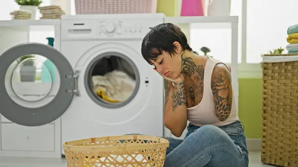 Hispanic woman with amputee arm washing clothes sitting on floor tired at laundry room