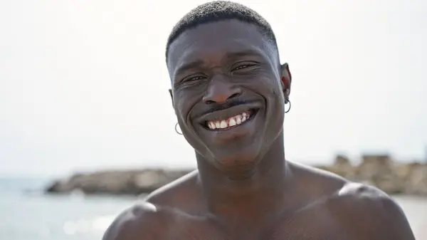 African american man tourist smiling confident standing shirtless at the beach