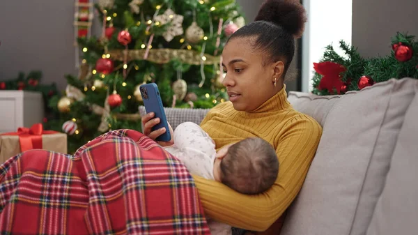 自宅で赤ちゃんを授乳しながらスマートフォンでクリスマスを祝う母と息子 — ストック写真