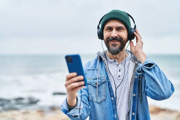 Young bald man smiling confident listening to music at seaside