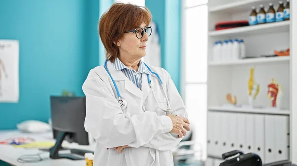 Middle age woman doctor standing with serious expression and arms crossed gesture at clinic