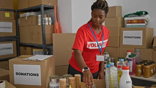 African american woman volunteer putting products in cardboard box at office