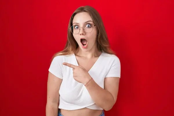 Young Caucasian Woman Standing Red Background Surprised Pointing Finger Side — Stock Photo, Image