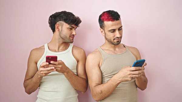 Two men couple using smartphones with relaxed expression over isolated pink background