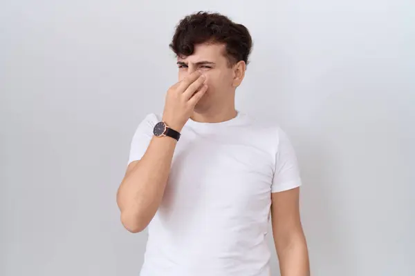 カジュアルな白いTシャツを着た若い非バイナリ男性は 臭いと嫌な 耐え難い匂いを嗅ぎ 鼻に指で息を止めています 悪い匂いがする — ストック写真