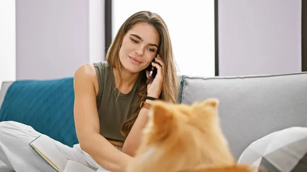 年轻的惊慌失措的女人带着狗在电话里坐在沙发上 — 图库照片