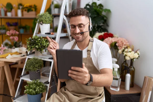 Hispanic man with beard working at florist shop doing video call smiling happy pointing with hand and finger to the side