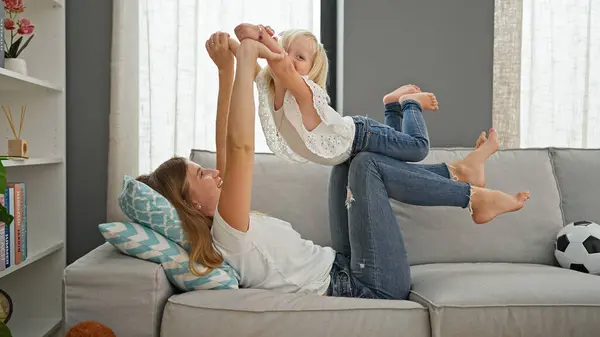 Confident caucasian mother and daughter lying comfortably on a sofa, playing and smiling in the warmth of their home