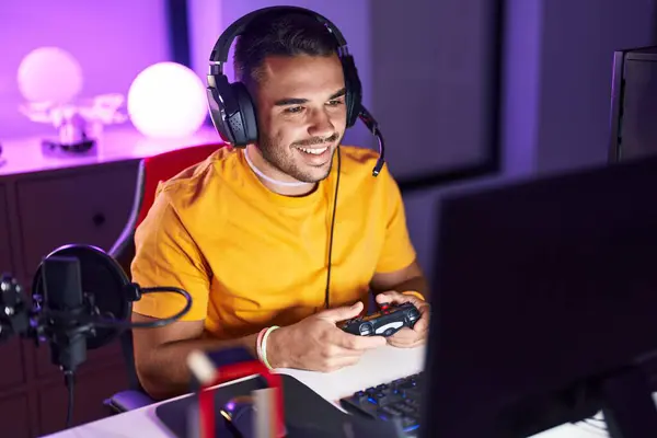 Young hispanic man streamer playing video game using joystick at gaming room