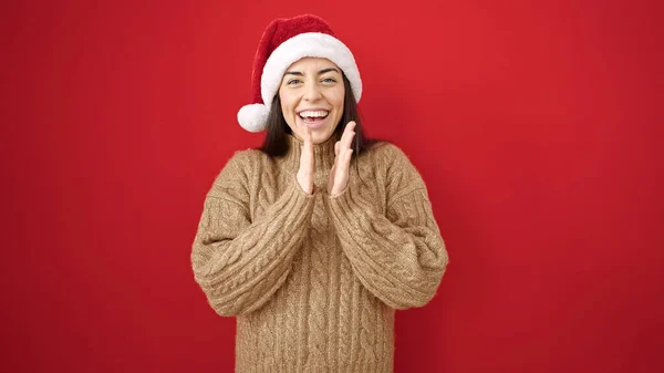 若い美しいヒスパニックの女性は 孤立した赤い背景の上に手をクラッピングクリスマスの帽子をかぶっています — ストック写真