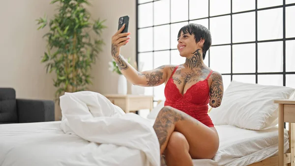 Hispanic woman with amputee arm wearing lingerie sitting on bed make selfie by smartphone at bedroom