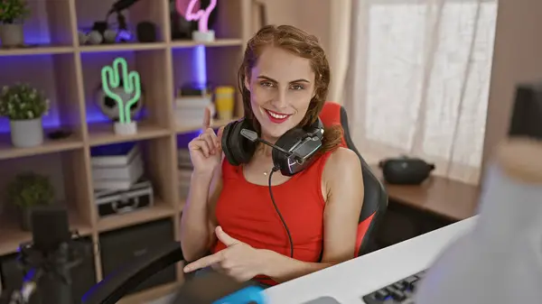 Check it out, confident young woman streamer points you out, taking off headphones amidst night's gaming stream in home office room