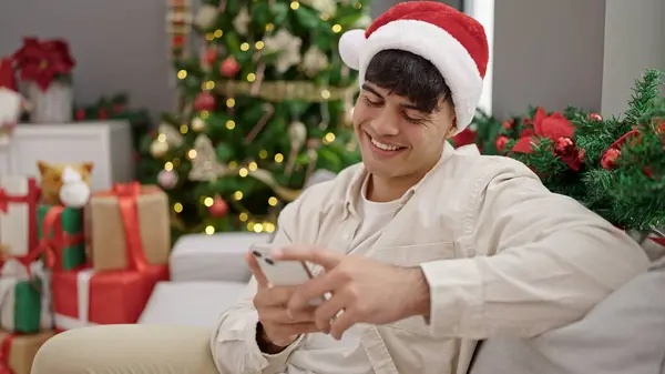 若いですヒスパニック男使用スマートフォンお祝いクリスマスに自宅 — ストック写真