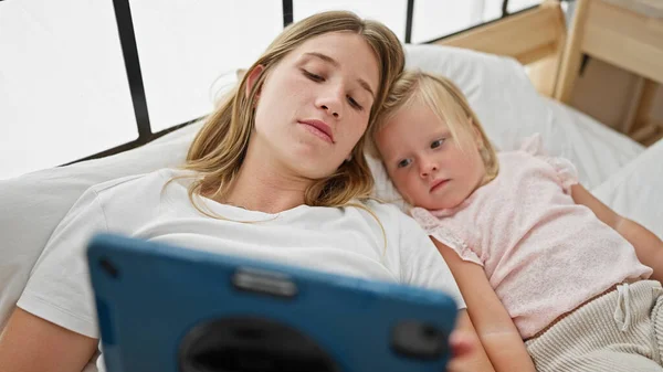 Caucasian mother and daughter lying on bed watching video on touchpad at bedroom