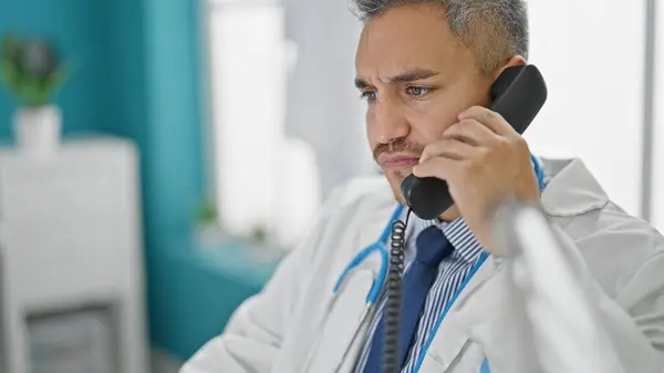 Young hispanic man doctor talking on telephone at clinic
