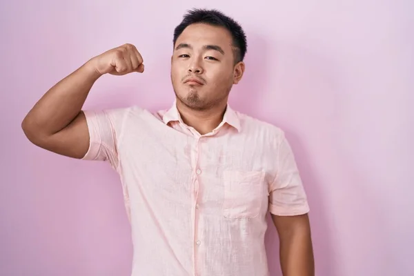 ピンクの背景の上に立っている中国の若者 腕の筋肉を示す強い人 自信と権力の誇り — ストック写真