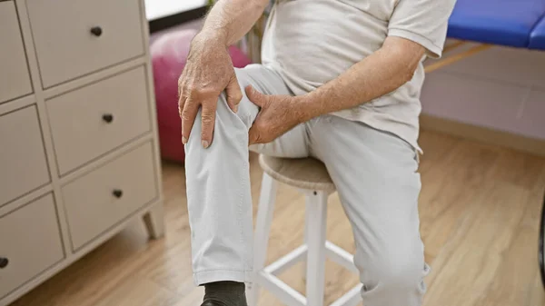 理学療法中のリハビリクリニックで苦しんでいる痛みのシニア男性の手触り膝 — ストック写真