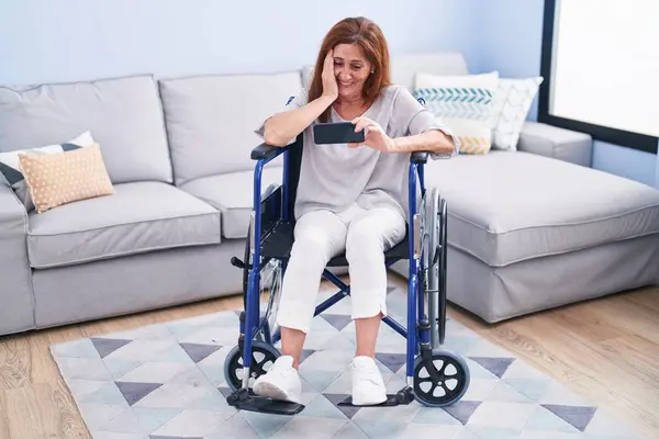 Evde Tekerlekli Sandalyede Oturan Orta Yaşlı Bir Kadın Akıllı Telefondan — Stok fotoğraf