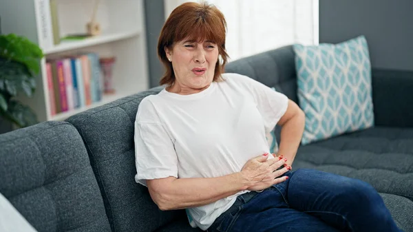 Middle age woman suffering for stomach ache sitting on sofa home