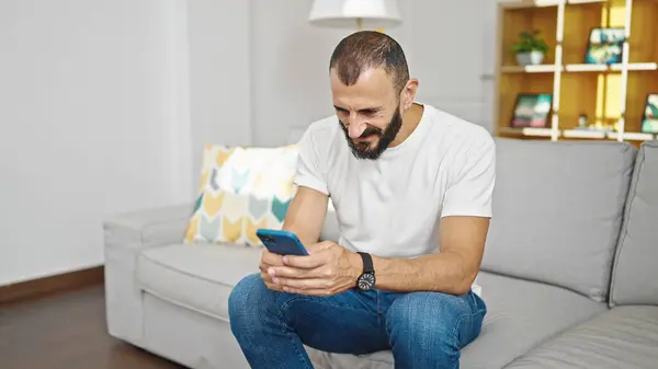 stock image Young hispanic man using smartphone sitting on sofa at home