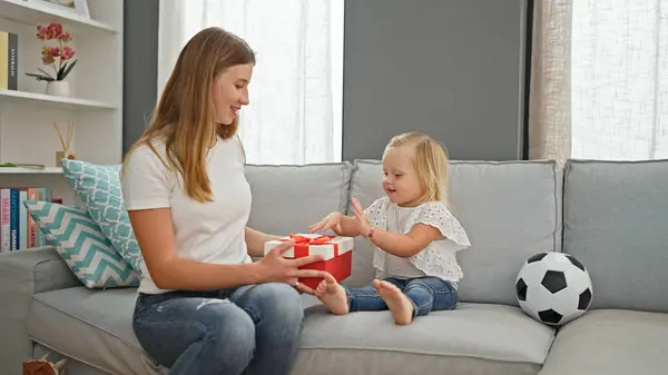 Caucasian mum and little girl surprising each other with birthday gifts, in the cozy living room of their home. two generations celebrating a special moment.