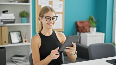 Ofiste gülümseyen dokunmatik ped kullanan genç sarışın iş kadını.