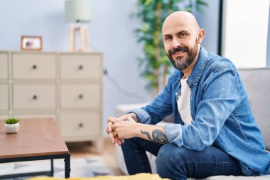 Young bald man smiling confident sitting on sofa at home