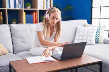 Kanepede oturan genç sarışın kız öğrenci evde ders çalışıyor.