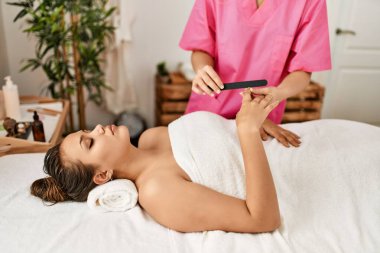Young beautiful hispanic woman lying on table having manicure treatment at beauty salon